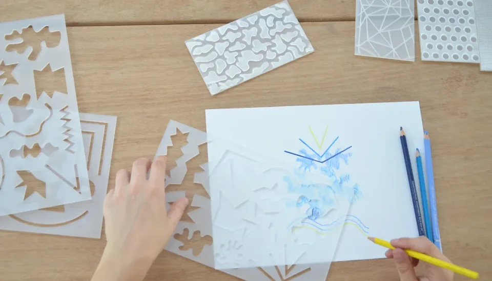 Mains dessinant aux crayons de couleur à l'aide des pochoirs du kit